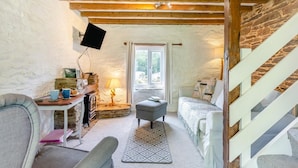 Un cuarto acogedor con pared de piedra, vigas de madera, chimenea, sofá, una mesa con tazas y una escalera.