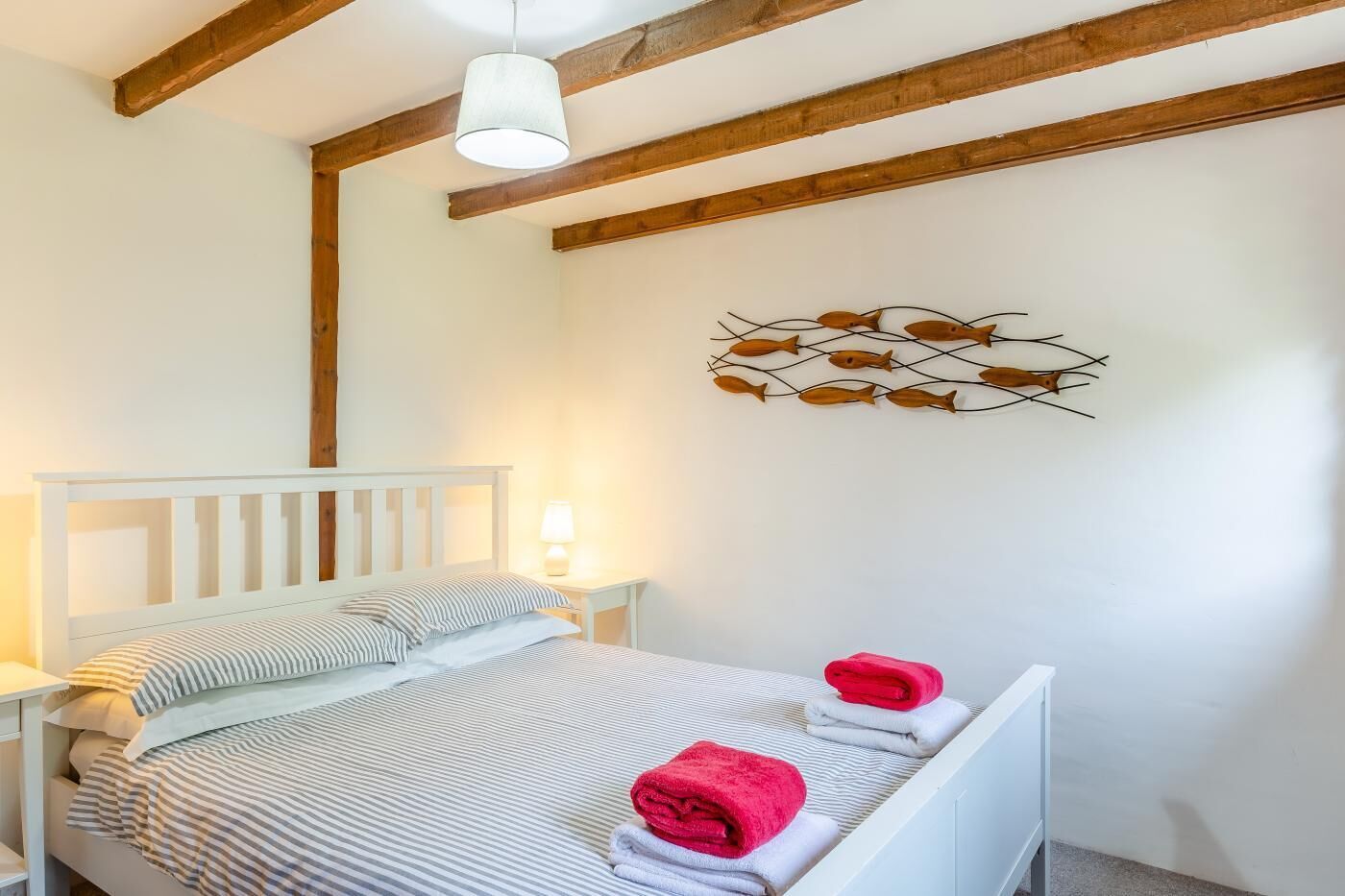 A bedroom with a white bed, striped bedding, and a wooden ceiling beam.