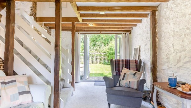 Una habitación acogedora con una escalera de madera, un sillón cómodo y vistas a un jardín a través de un ventanal.