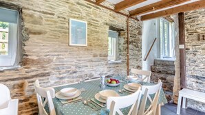 Interior rústico de piedra con una mesa de comedor para cuatro personas, rodeada de sillas blancas.