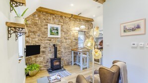 A cozy living room with a stone wall, a fireplace, a dining area, and a comfortable seating area. - 1 Bed in Drumnadrochit (oc-t32404) (Drumnadrochit)