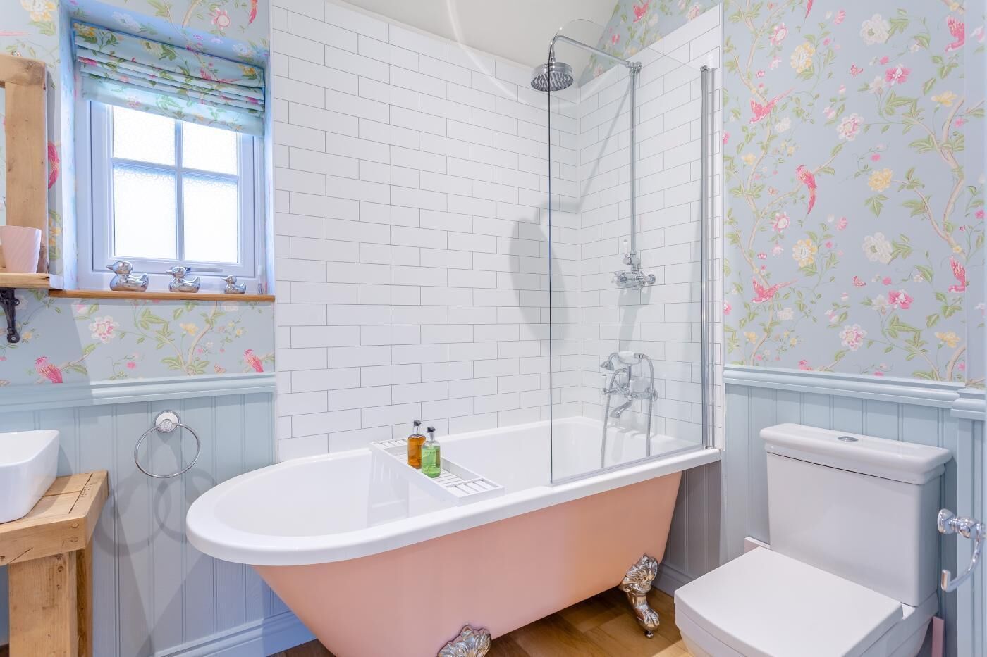 Un bagno con una vasca freestanding, una doccia vetrata, un water e una finestra con tenda a fiori.