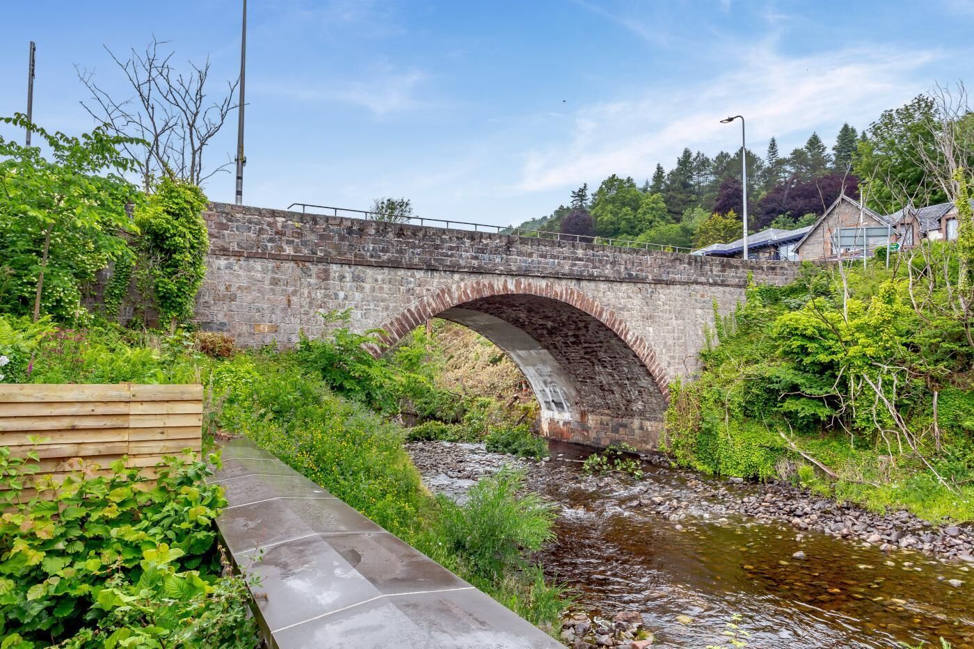 A stone bridge over a stream with a wooden walkway on one side.