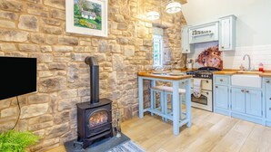 A rustic kitchen with a stone wall, a wood-burning stove, a wooden table, and light blue cabinets. - 1 Bed in Drumnadrochit (oc-t32404) (Drumnadrochit)