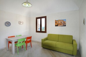 Ein Essbereich mit Tisch und Stühlen, einem grünen Sofa, einem Fenster mit Aussicht und einer dekorativen Leuchte.