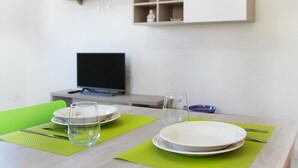 Et spisebord med tallerkener, glas og bestik, et fjernsyn i baggrunden og en hylde over bordet.