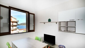 Ein kleiner, heller Raum mit einem Holztisch, einem Fernseher und Meerblick durch ein Fenster.