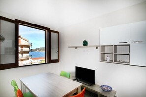 Una habitación pequeña y luminosa con una mesa de madera, un televisor y vista al mar a través de una ventana.