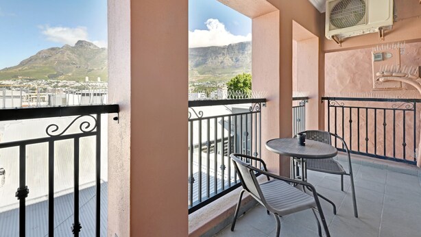 A balcony with a table and chairs, a view of a mountain, and an air conditioning unit.