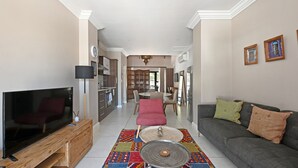 A spacious living room with a flat-screen TV, a sofa, and a dining area in the background.