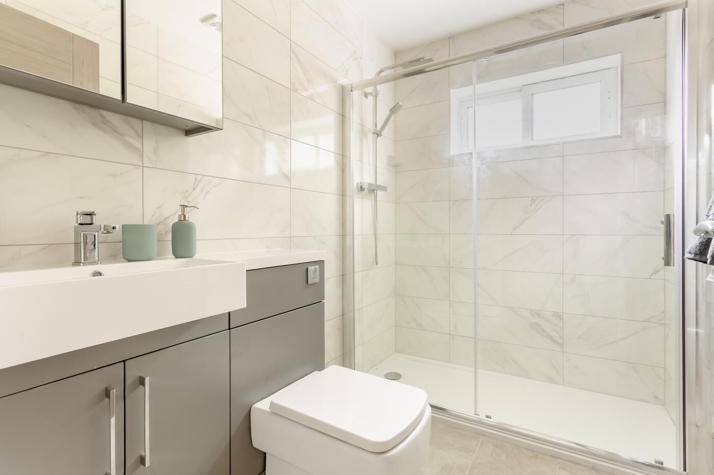 A modern bathroom with a glass shower enclosure, a white toilet, and a vanity with a mirror and storage.