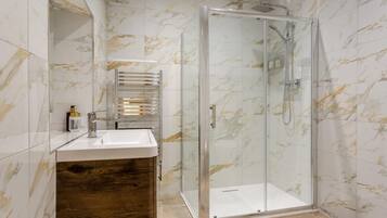 A modern bathroom with a glass-enclosed shower, a wooden vanity, and marble-patterned walls.