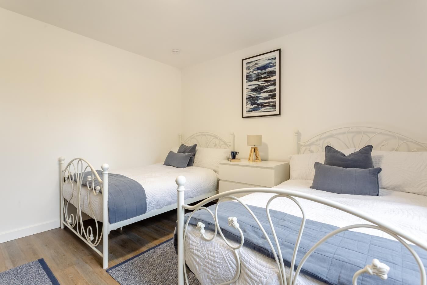 A bedroom with two beds, a nightstand, a lamp, and a framed picture on the wall.