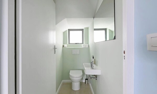 A small, narrow bathroom with a toilet, sink, and a window above the toilet. - Spacious Family Camps Bay Escape |  Spectacular Views | Pool, Garden (Cape Town)
