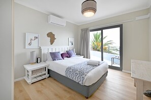 A modern bedroom with a large bed, a bedside table, a lamp, and a view of the outdoors. - Spacious Family Camps Bay Escape |  Spectacular Views | Pool, Garden (Cape Town)