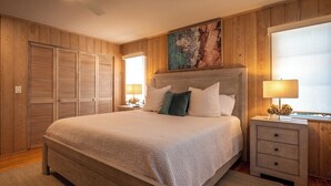 Ein Schlafzimmer mit einem großen Bett, Holzwandverkleidung, einem Bild über dem Bett und einem Nachttisch mit einer Lampe.