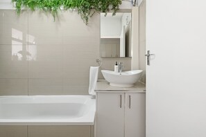 A modern bathroom with a bathtub, a sink, a mirror, and a plant. - Charming Central Sea Point Haven | 50m to Ocean (Cape Town)