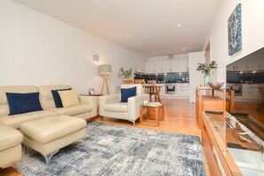 Ein modernes Wohnzimmer mit Sofa, Sesseln, Couchtisch und einer Essecke mit Tisch und Stühlen.