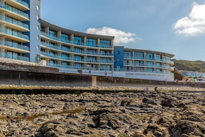 Ein mehrstöckiges Hotel mit Balkonen, einer felsigen Küstenlinie und einem klaren Himmel.