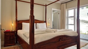 Ein Bett mit Baldachin, ausgestattet mit weißen Leintüchern, ein Nachttisch aus Holz mit einem roten Buch und ein gemustertes Teppich.