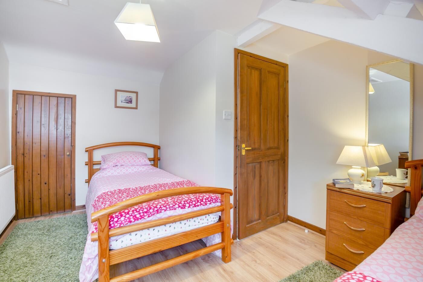 A bedroom with a wooden bed, a dresser, a mirror, and a door.