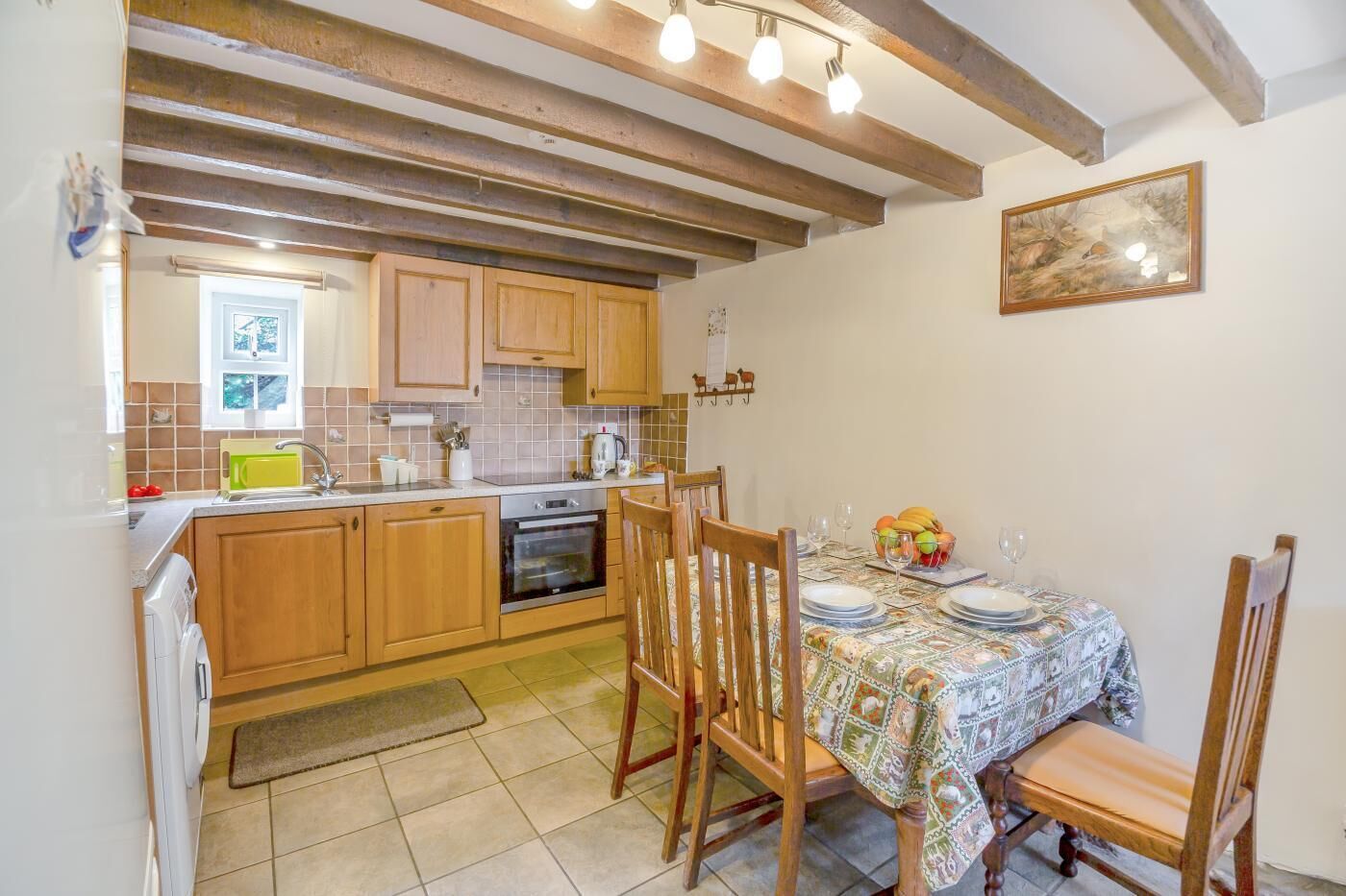 A kitchen with wooden cabinets, a dining table with a patterned tablecloth, and a hanging light fixture.