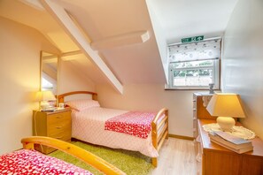 A bedroom with a bed, bedside table, lamp, dresser, and a window with a view.