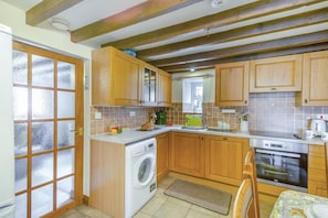 A compact kitchen with wooden cabinets, a washing machine, a sink, and a stove. - 2 Bed in Llanbedrog (oc-r32641) (Llanbedrog)