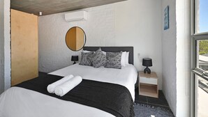 Ein Schlafzimmer mit einem Bett, zwei Nachttischen, einem runden Spiegel und einem Fenster.