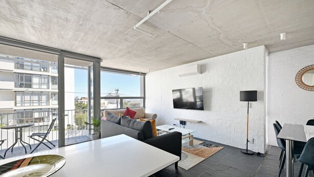 Ein modernes Wohnzimmer mit großem Fernseher, einer Couch, einem Essbereich und einem Balkon mit Blick auf die Stadt.
