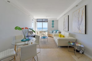 Una sala moderna con una mesa de comedor de vidrio, sofás blancos y vista al océano.