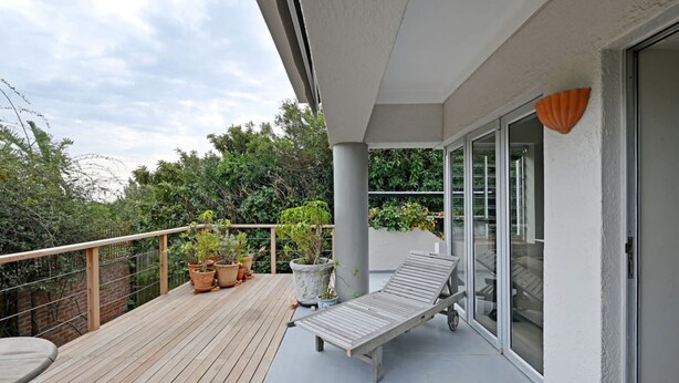 Eine Holzterrasse mit Liegestuhl und Kübelpflanzen, eine Glastür und Blick ins Grüne.