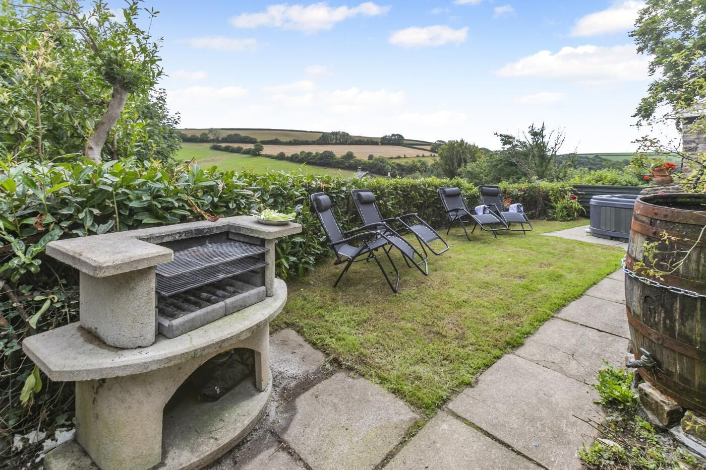 A garden with a barbecue grill, outdoor seating, and a view of rolling hills.
