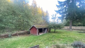 A rustic barn with a shed, surrounded by a grassy area and trees.