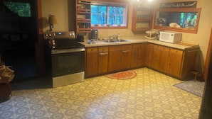 A kitchen with wooden cabinets, a stove, a microwave, and a window with a view of trees.