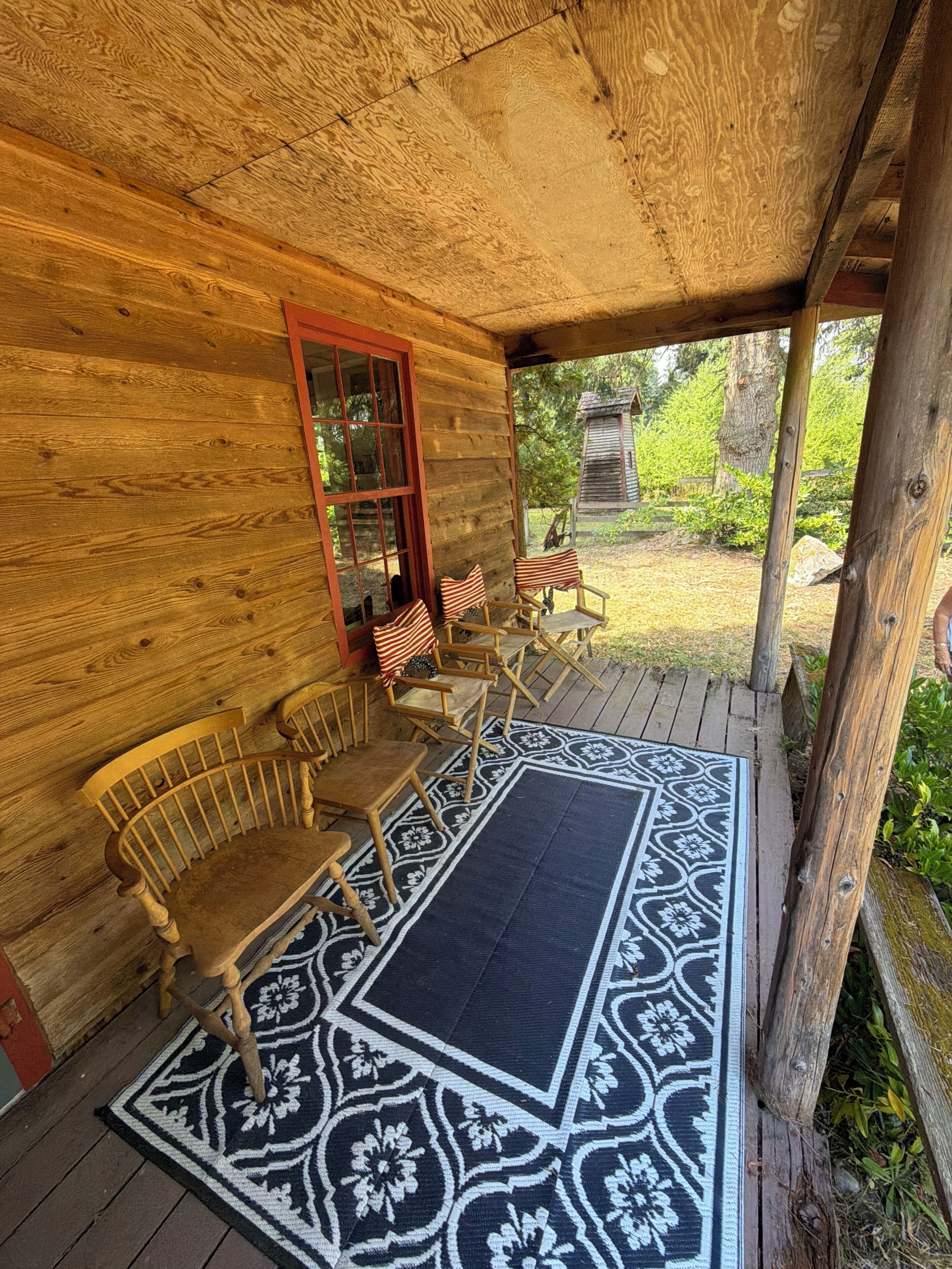 Une cabane en bois dotée d’un porche, meublée de chaises et d’un banc en bois, et agrémentée d’un tapis à motifs.