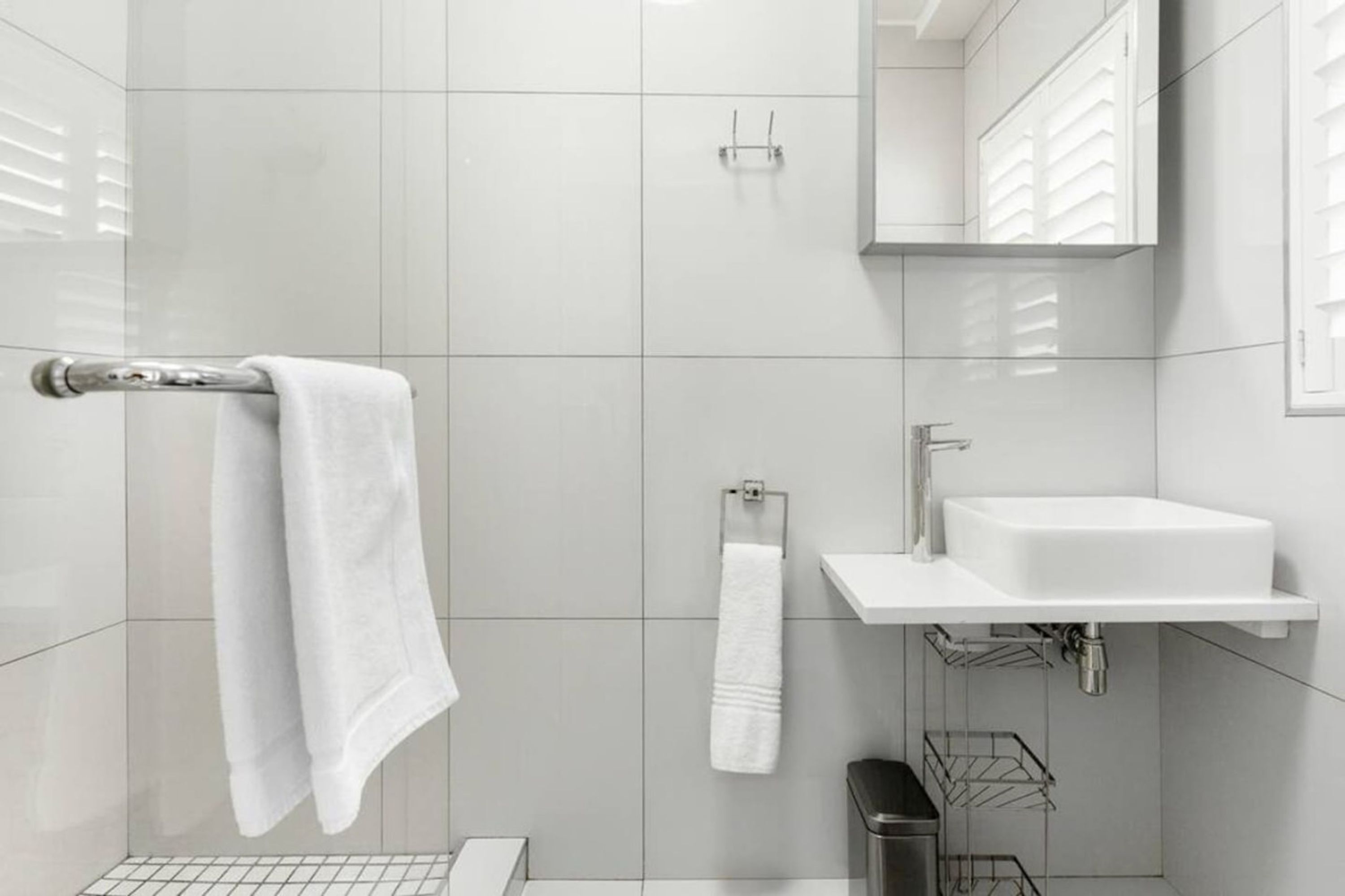 Une salle de bain moderne avec un lavabo blanc, un miroir et un porte-serviettes.