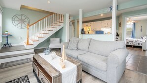 Un salon avec un escalier, un canapé, une table basse et une cuisine en arrière-plan.