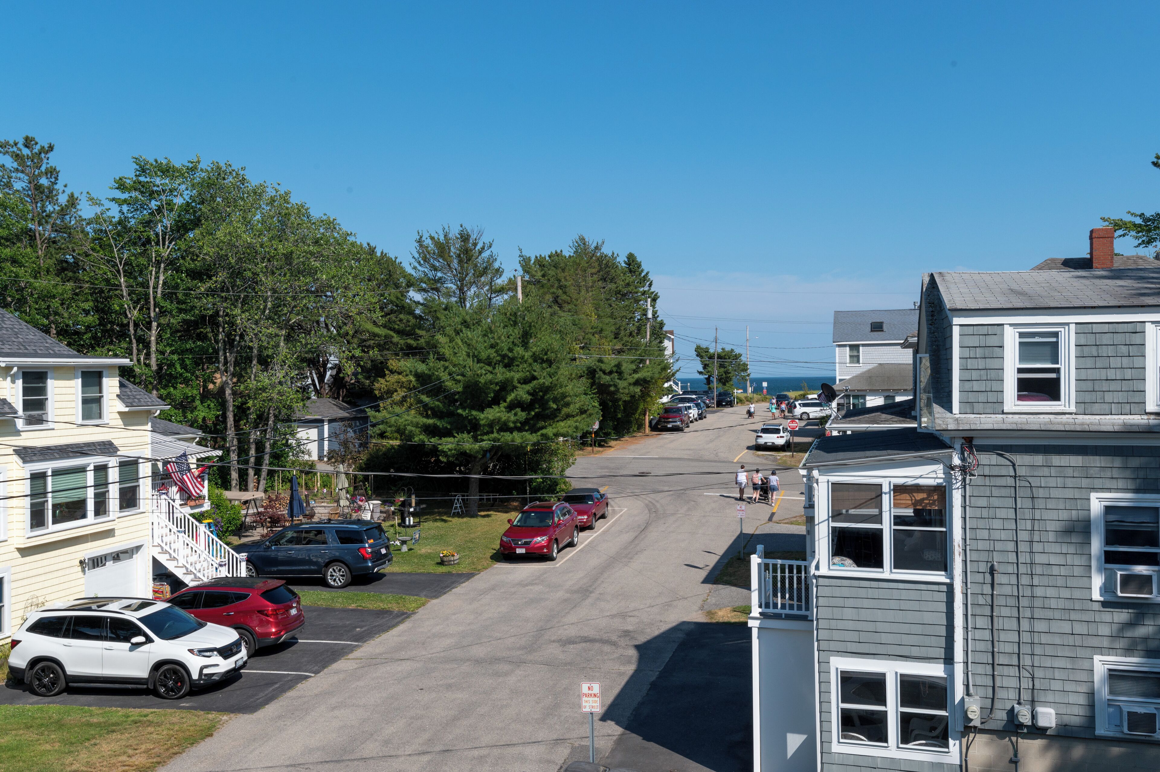 A residential street with houses, parked cars, and a clear sky.