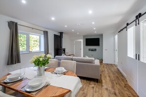 Een moderne woonkamer met een bank, een eettafel gedekt voor twee personen, en een open haard.