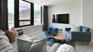 Ein modernes Wohnzimmer mit großem Fenster, einem Flachbildfernseher, einer Couch, einem Couchtisch und blauen Ottomanen.