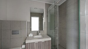 Ein modernes Badezimmer mit Duschkabine aus Glas, einem Waschbecken mit Marmorplatte und einem Holzwaschtisch.