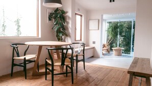 Een modern interieur met een houten eettafel, zwarte stoelen, een potplant en uitzicht op groen door een groot raam.