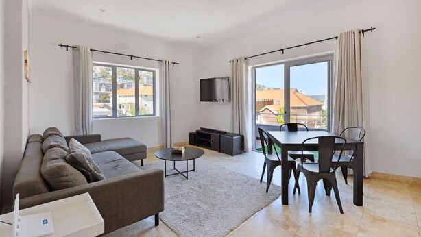 Una sala de estar moderna con sofá, mesa de centro, televisión y comedor con sillas y mesa.