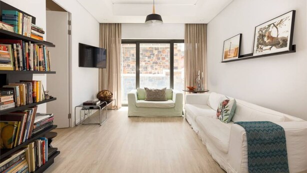 Een moderne woonkamer met een witte bank, een boekenkast, een flatscreen-tv en een groot raam met uitzicht over de stad.
