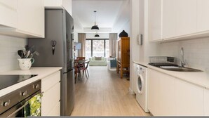 Een moderne keuken met witte kasten, een roestvrijstalen koelkast, een wasmachine en een eethoek met een tafel en stoelen.