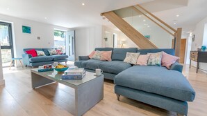 Ein modernes Wohnzimmer mit Ecksofa, Glastisch und einer Treppe mit Holzbalken.