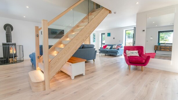 Ein modernes Interieur mit einer Holztreppe, einem Kamin, einem blauen Sofa, einem roten Sessel und einem Holzboden.