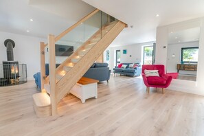 A modern interior with a wooden staircase, a fireplace, a blue sofa, a red armchair, and a wooden floor. - 3 Bed in Poundstock (oc-a32920) (Poundstock)