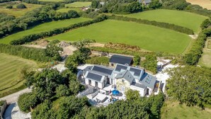 Ein weitläufiges Anwesen mit ausgedehnten grünen Feldern, einem Schwimmbad und einem modernen Haus mit mehreren Ebenen und großen Fenstern.